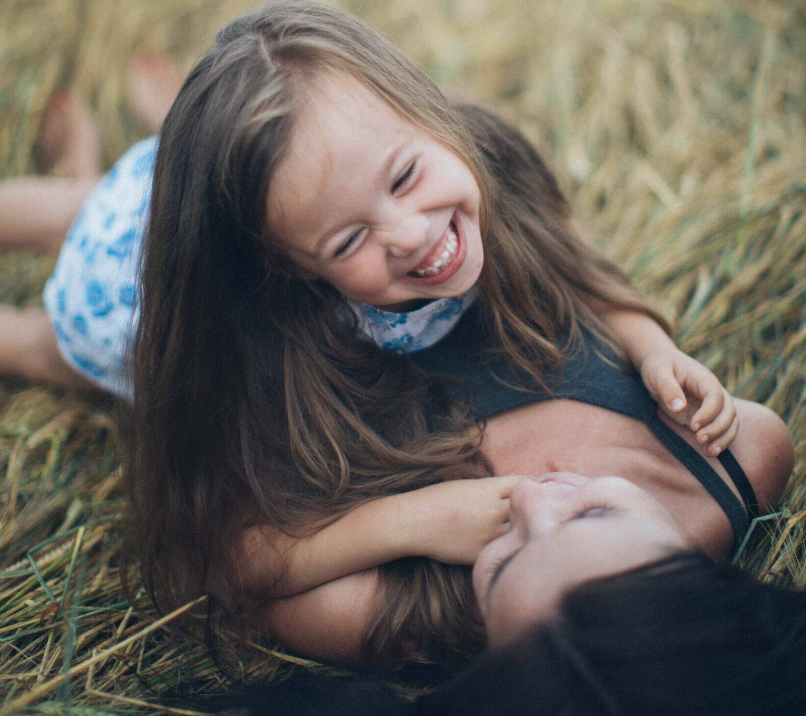 Mom lying on back laughing with daughter in grass