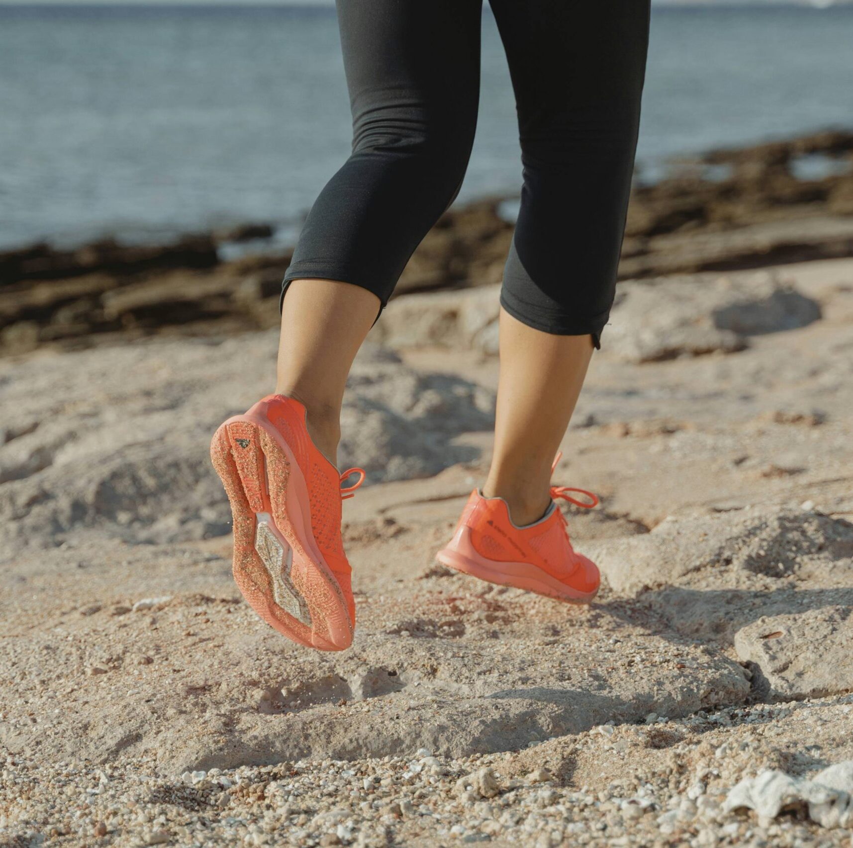 Women's legs running on sand by beach