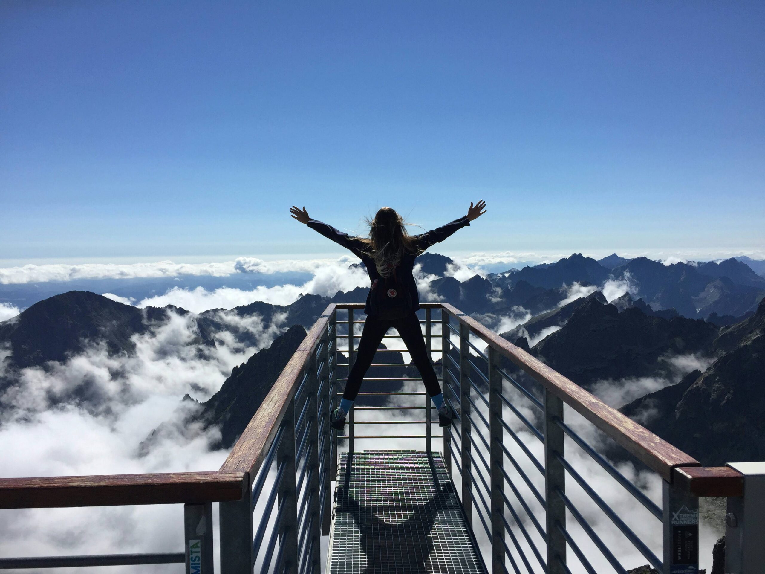 Strong woman with arms stretched out on top of mountain